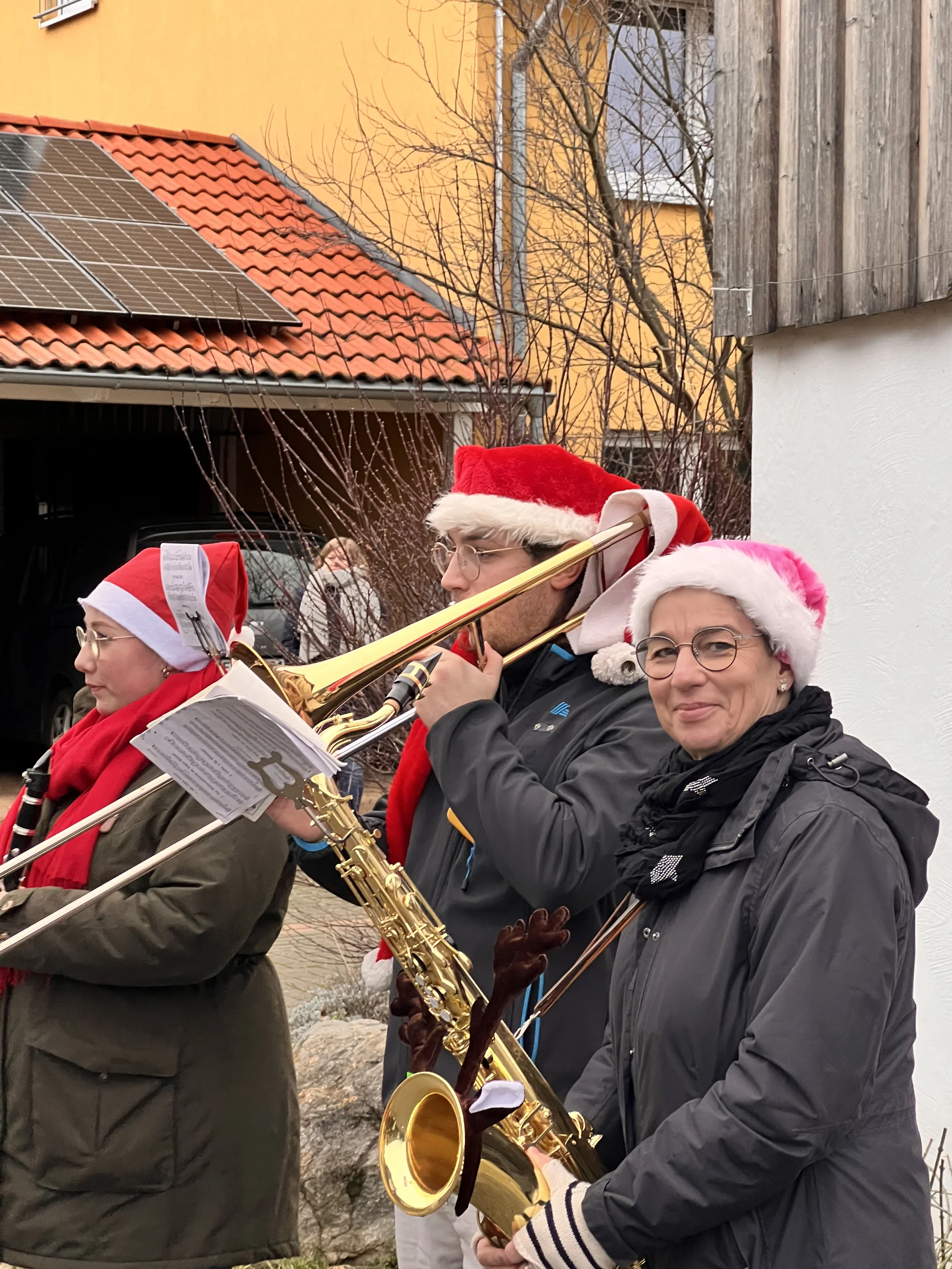Musikerinnen und Musiker mit Weihnachtsmützen spielen Posaune und Saxophon bei den Weihnachtsliedern im Dorf