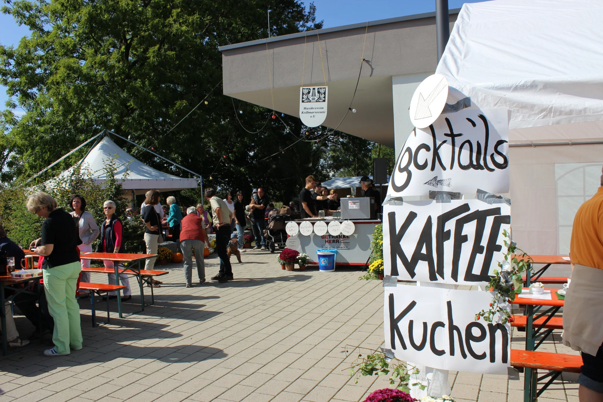 Dorffest mit Biertischen, Zelt und handgeschriebenen Schildern für Kaffee, Kuchen und Cocktails