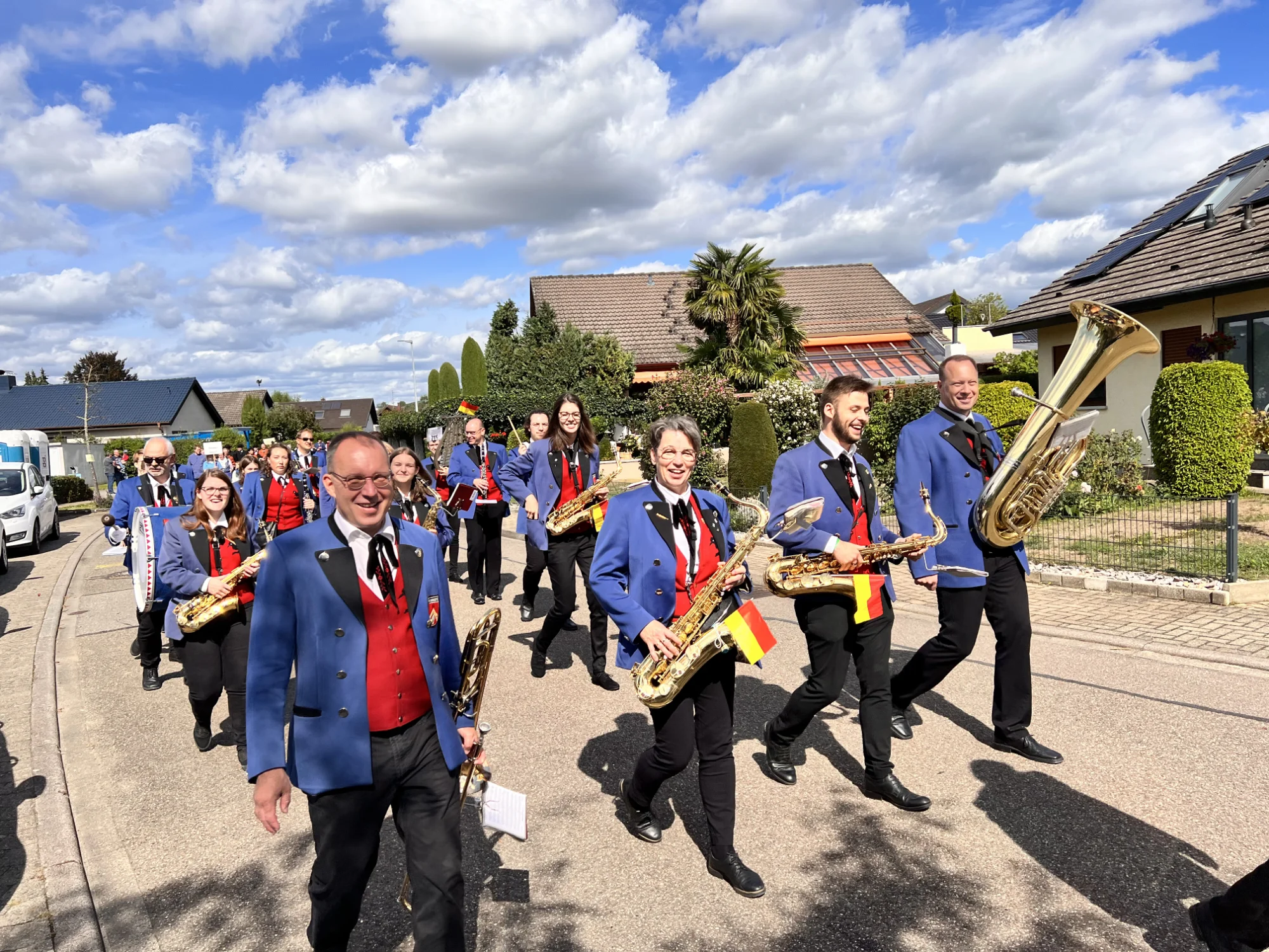 Die Musikkapelle in blauen Jacken und roten Westen zieht mit Saxophonen und Tuba beim Winzerfest in Auggen durch die Straße
